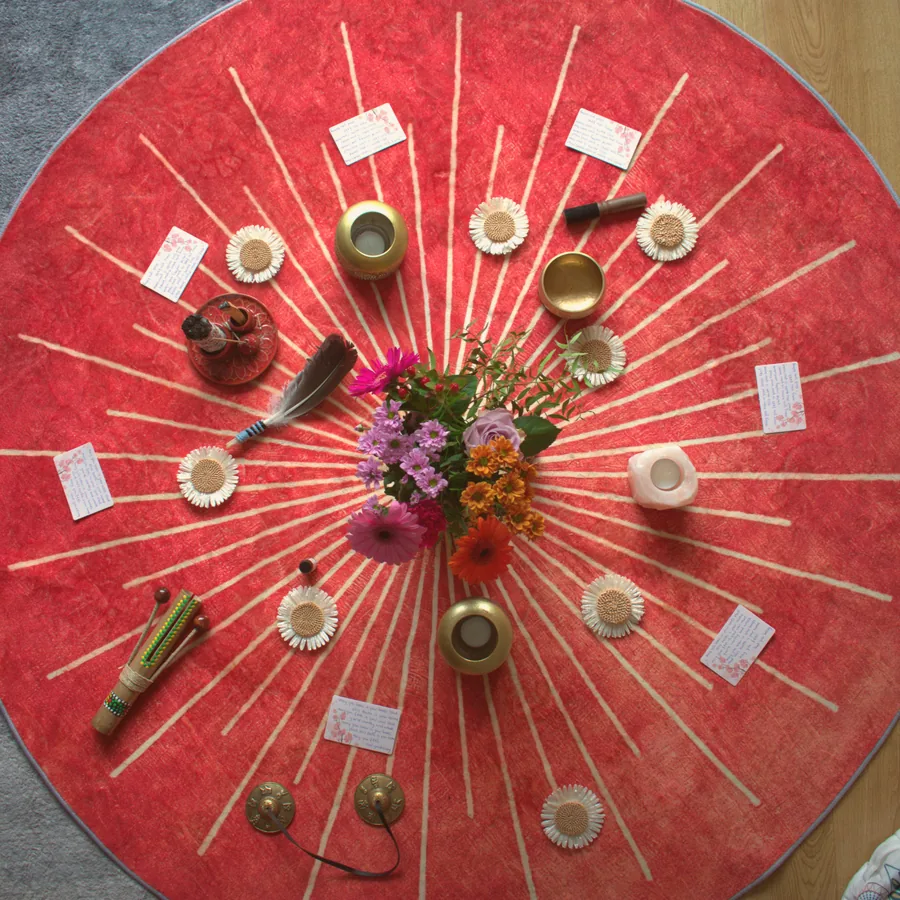 Een cirkel met schalen, kaarsen en bloemen op een rode doek.